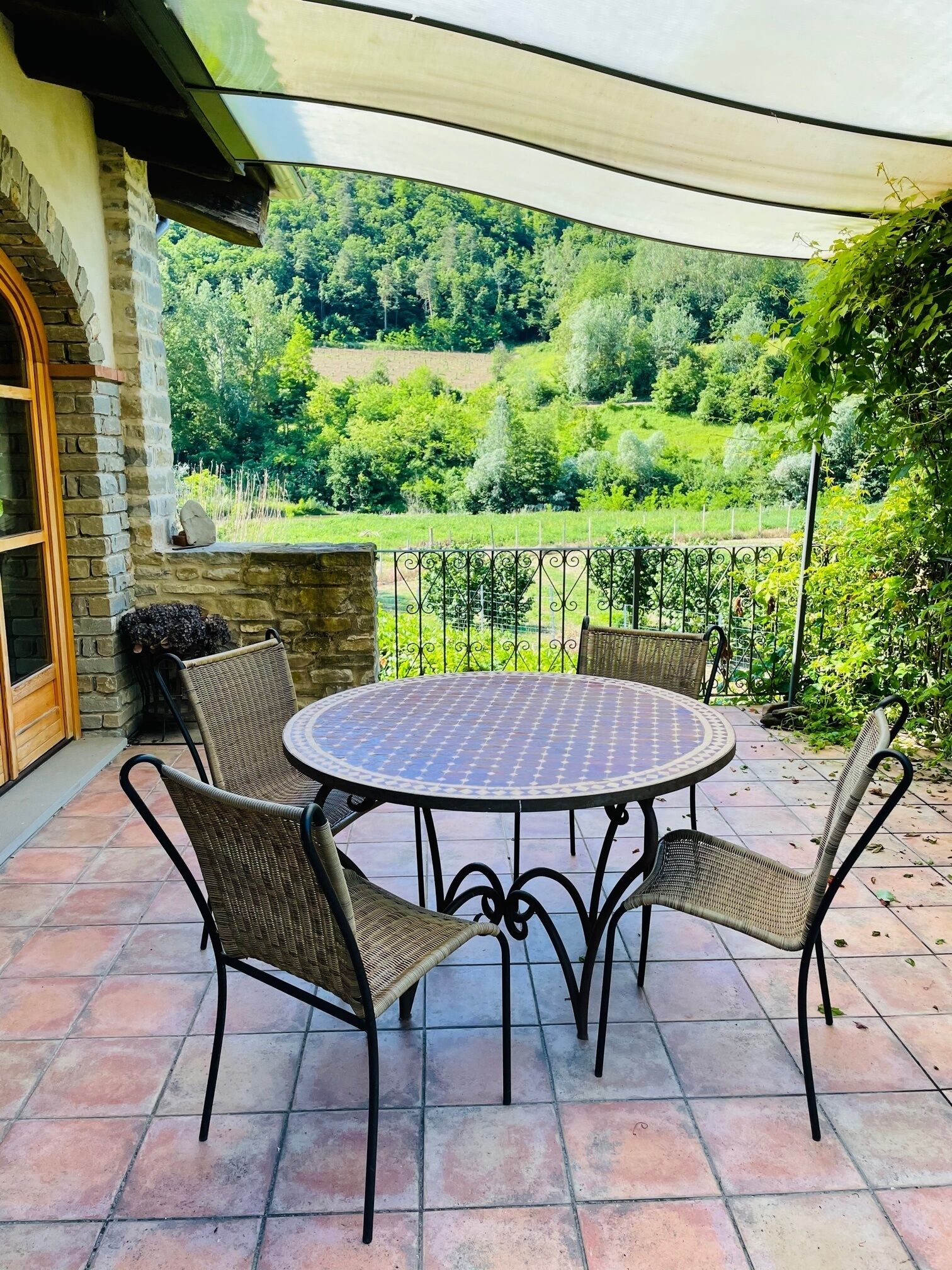 Un patio con una mesa redonda y cuatro sillas de mimbre, rodeado por un muro de piedra y una valla de metal.