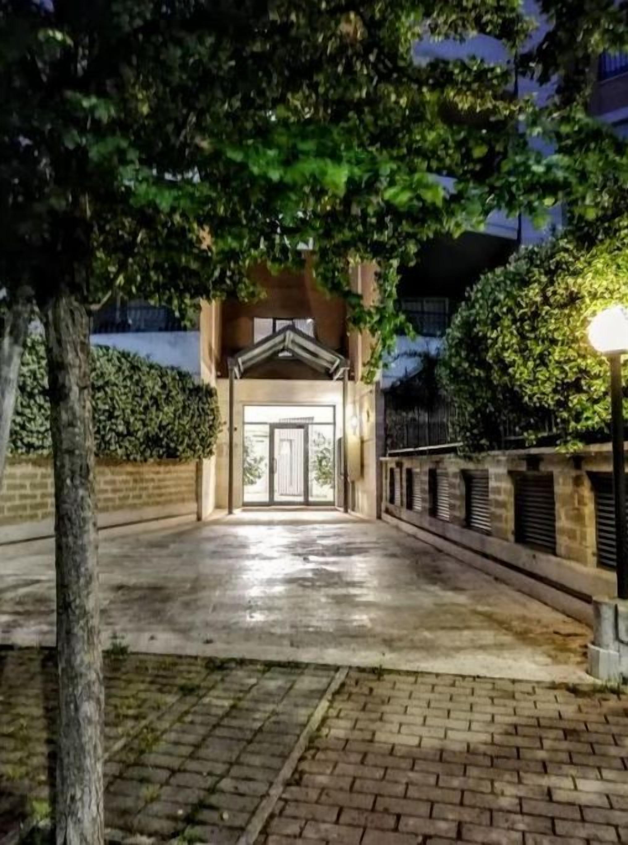 A pathway leading to a building entrance at night, flanked by trees and a brick wall.