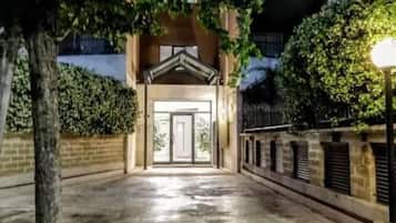 A pathway leading to a building entrance at night, flanked by trees and a brick wall.