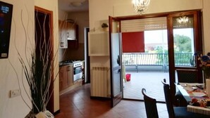 Eine Küche mit Herd, Backofen und Schränken, die auf einen Balkon mit roter Markise und Blick ins Freie führt.