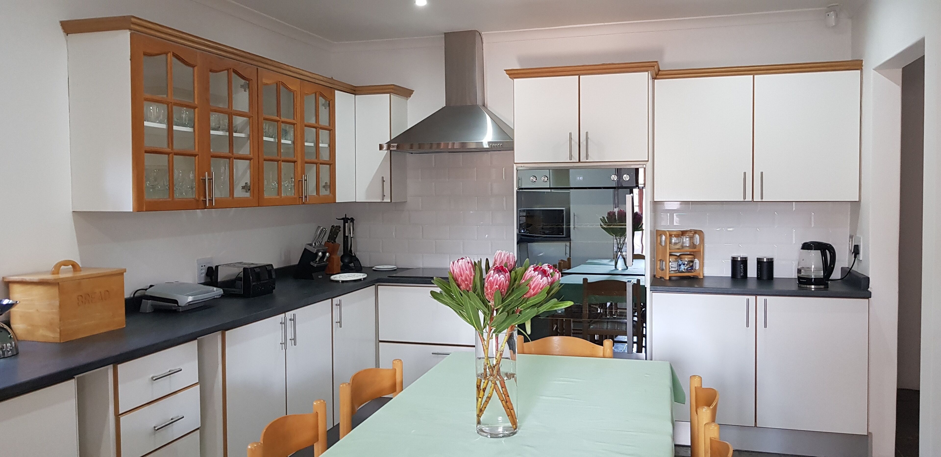 Una cocina con gabinetes blancos, horno empotrado y un comedor con mesa y sillas.
