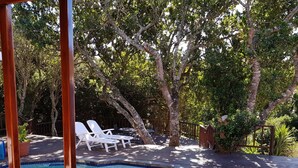 Una piscina con borde de azulejos, rodeada por una terraza de madera y sillas reclinables blancas.