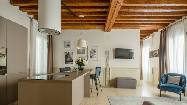 A modern kitchen with a central island, bar stools, and a dining area with a TV mounted on the wall. - Lion Palace Superior R&R (Venecia)