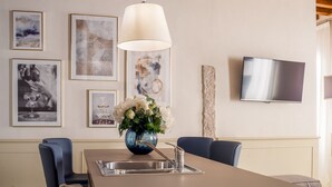A dining area with a table, chairs, a vase of flowers, a hanging lamp, and framed artwork on the wall. - Lion Palace Superior R&R (Venecia)
