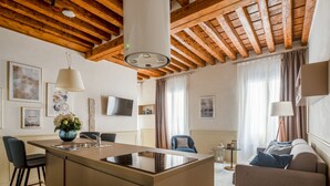 A modern kitchen with a central island, wooden ceiling beams, and a flat-screen TV on the wall. - Lion Palace Superior R&R (Venecia)