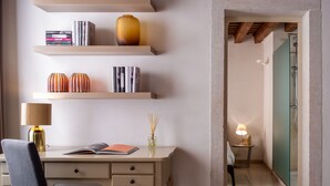 A room with a desk, shelves with books and decorative items, a chair, and a bathroom with a shower and a mirror. - Lion Palace Junior Suite R&R (Venecia)