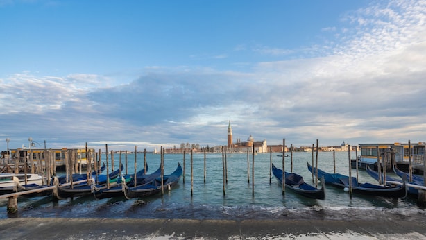 A waterfront with gondolas docked at a pier, a historic building in the background, and a clear sky. - Lion Palace Junior Suite R&R (Venecia)