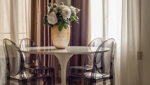 A dining area with a round table, clear chairs, a vase of flowers, and a hanging light fixture. - Lion Palace Junior Suite R&R (Venecia)