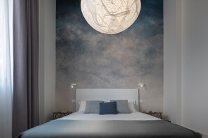 Quarto com uma cama grande, duas mesas de cabeceira e um mural na parede com uma lua.