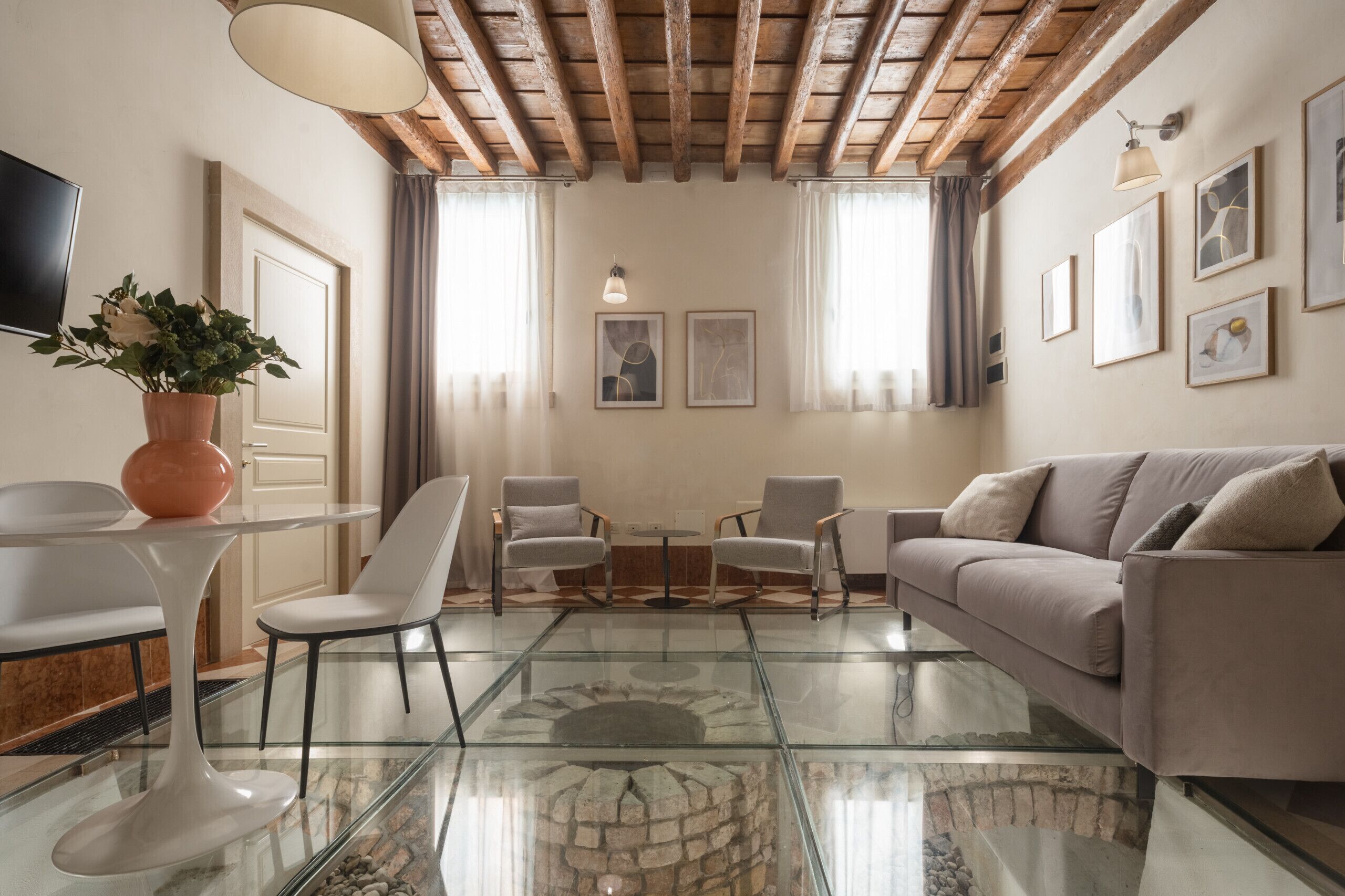 Un salón moderno con una mesa de centro de cristal, sillas blancas, un sofá color beige y una chimenea de piedra.