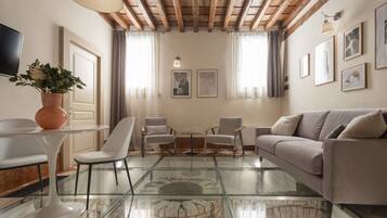 Un salón moderno con una mesa de centro de cristal, sillas blancas, un sofá color beige y una chimenea de piedra.