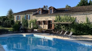 Une grande maison avec une piscine, un espace extérieur aménagé et un mur en pierre.