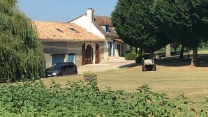 Une maison avec un toit en tuiles, une voiture garée devant et une pelouse avec un banc.