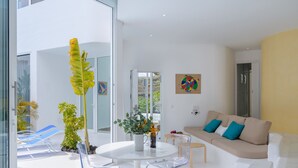 Un salón moderno con un sofá beige, sillas traslúcidas, una mesa blanca y una planta en maceta.
