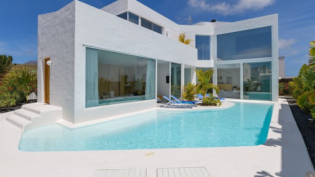 Una casa moderna de dos pisos con piscina, amplios ventanales y fachada blanca.