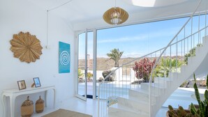 Ein modernes Interieur mit einer Treppe zu einem Balkon, einem weißen Konsolentisch mit Dekoration und einem großen abstrakten Gemälde.