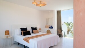 Ein modernes Hotelzimmer mit einem großen Bett, einem kleinen Nachttisch, einem Sessel und Blick ins Freie.