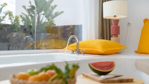 Une salle de bain avec un lavabo, un coussin jaune, une lampe blanche et un saladier de fruits.