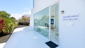 Un bâtiment moderne avec une entrée en verre, portant l’inscription « AQUABLANCA SUITE DELUXE », et un panneau indiquant la présence d’une piscine.
