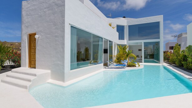 Un bâtiment moderne de couleur blanche, doté d’une piscine, de grandes fenêtres en verre et d’une porte.