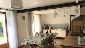 Uma sala de jantar com mesa posta para seis, cozinha com painel de azulejos e teto de madeira.