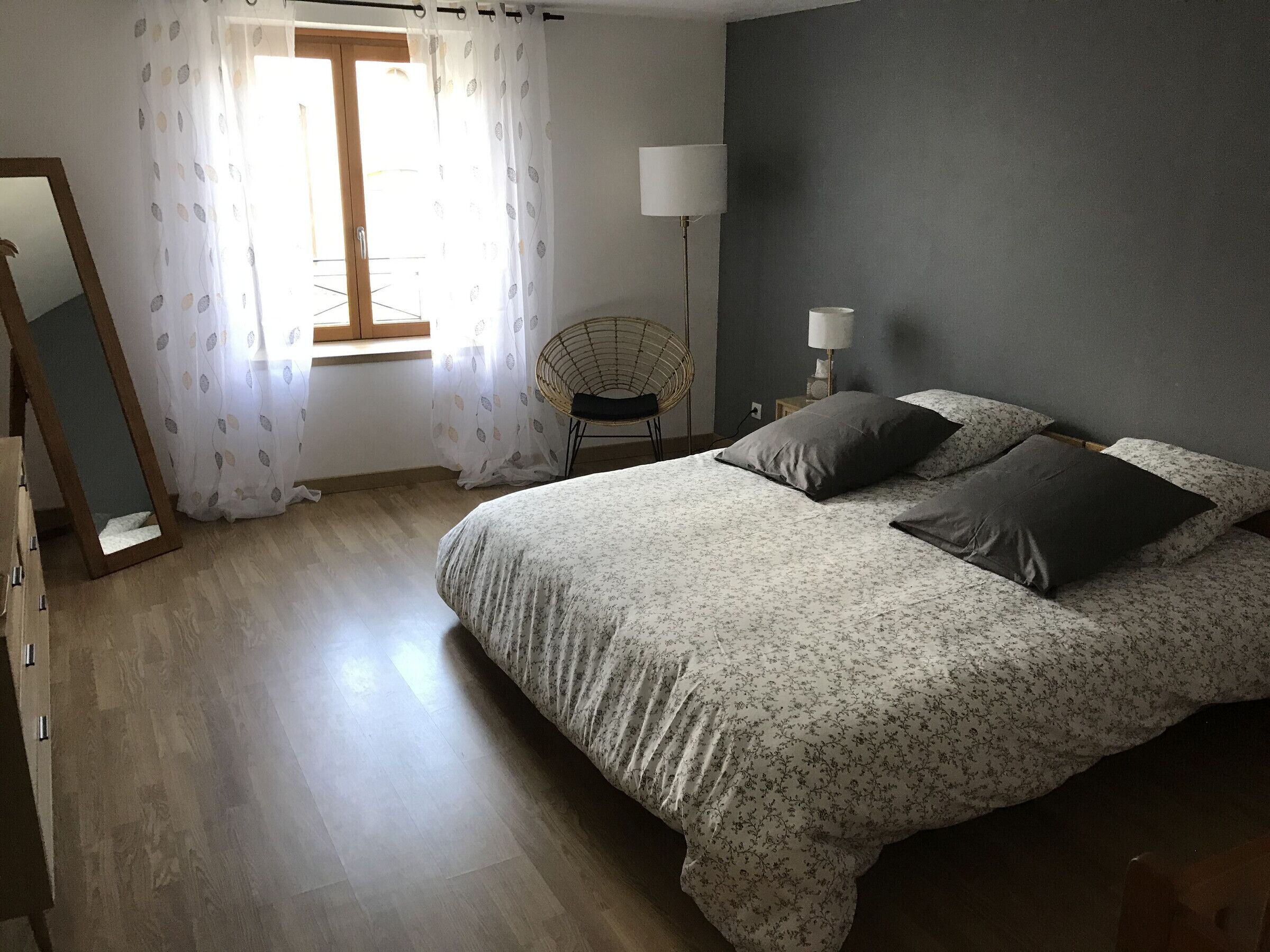 A bedroom with a large bed, a chair, a lamp, and a window with curtains.