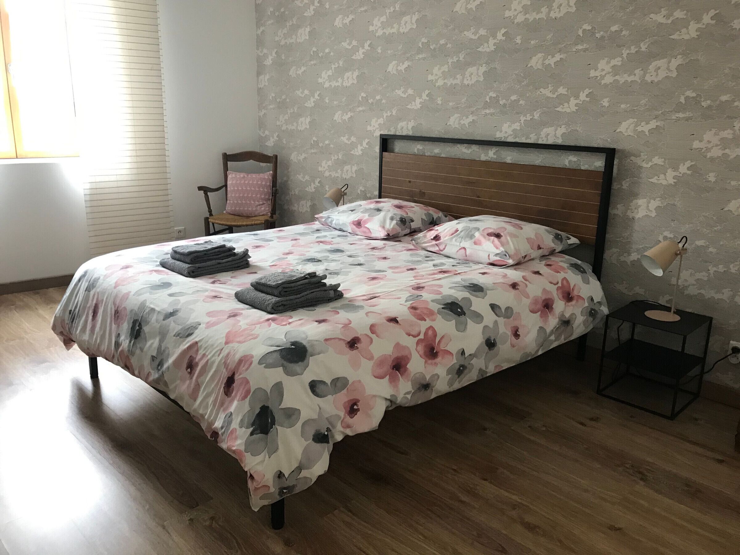 Una cama bien hecha con ropa de cama floral, un cabecero de madera y una lámpara de noche.