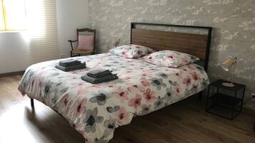 Una cama bien hecha con ropa de cama floral, un cabecero de madera y una lámpara de noche.