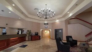Un vestíbulo de hotel con una recepción, una araña, una escalera y un área de descanso.