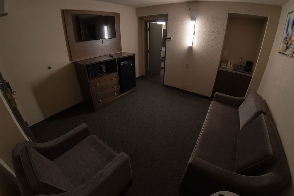 Een hotelkamer met een flatscreen televisie, een bureau met lades, een bank en een deur naar een andere kamer.