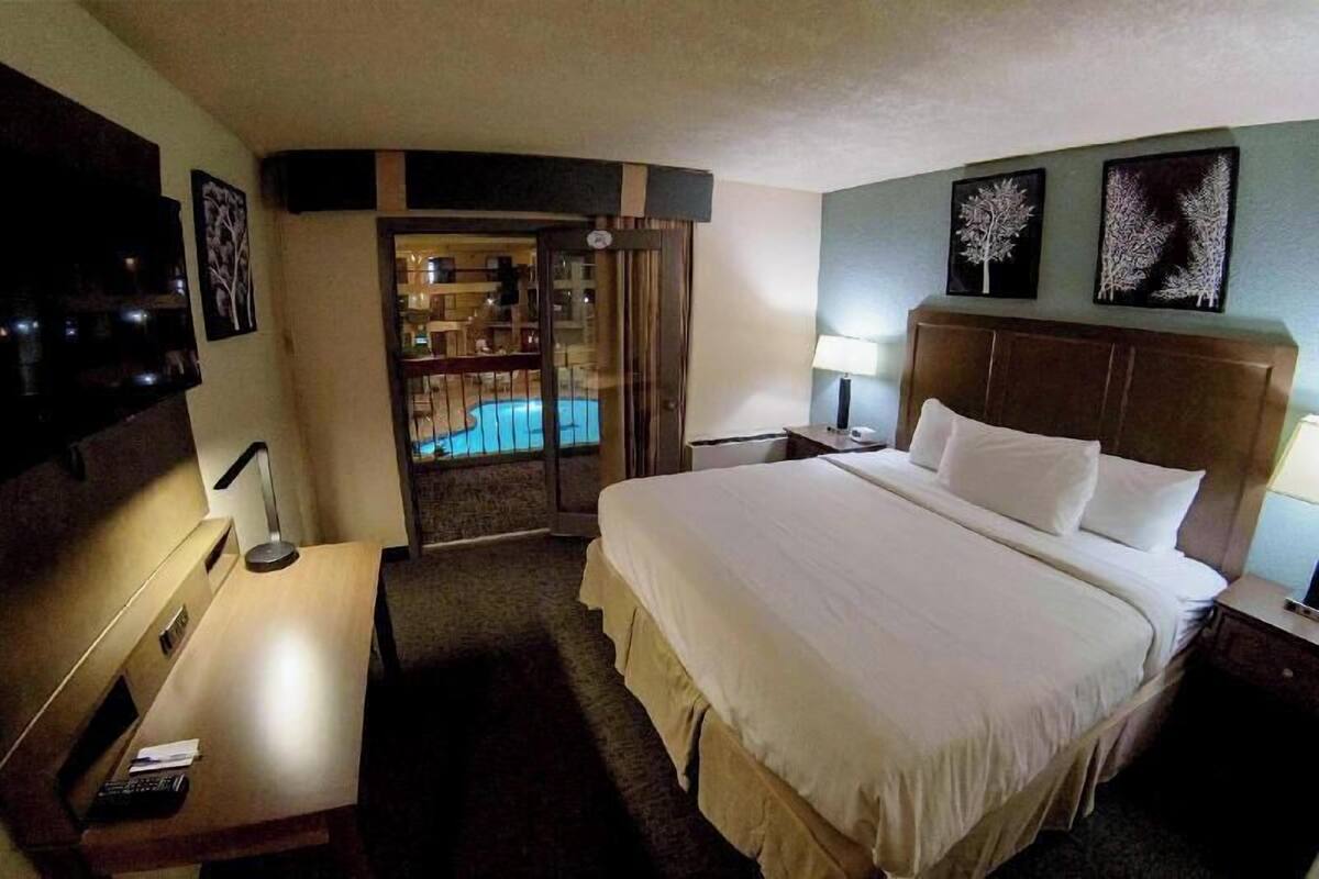 Een hotelkamer met een bed, bureau, lamp, televisie en uitzicht op een zwembad.