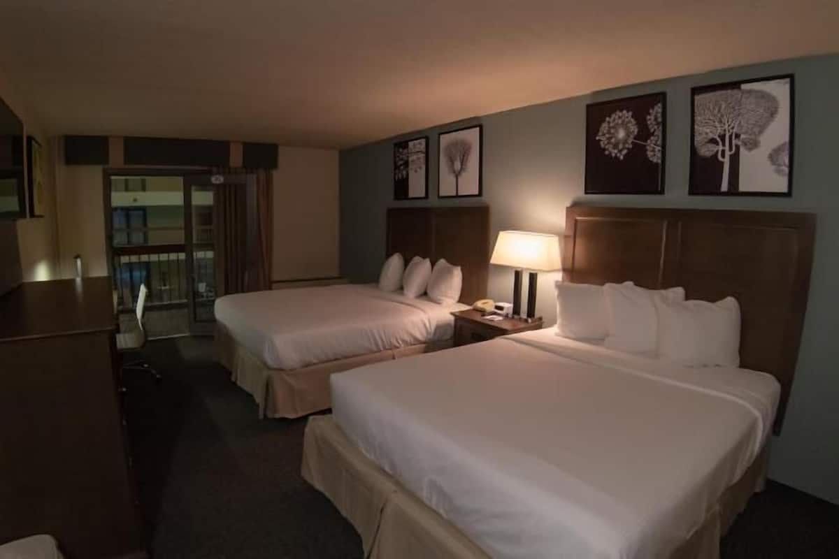 Een hotelkamer met twee bedden, een bureau, een stoel, een lamp en kunst aan de muur.