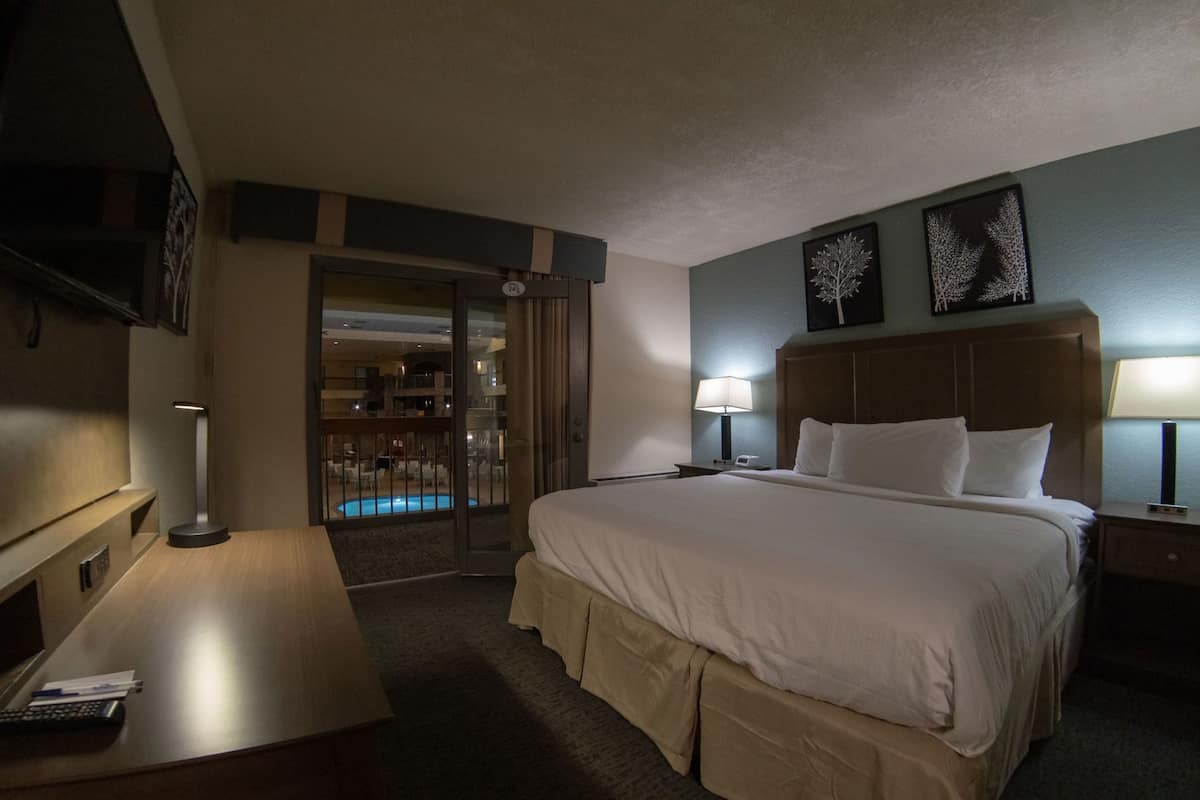Een hotelkamer met een bed, nachtlampen, een bureau, een televisie en uitzicht op een zwembad.