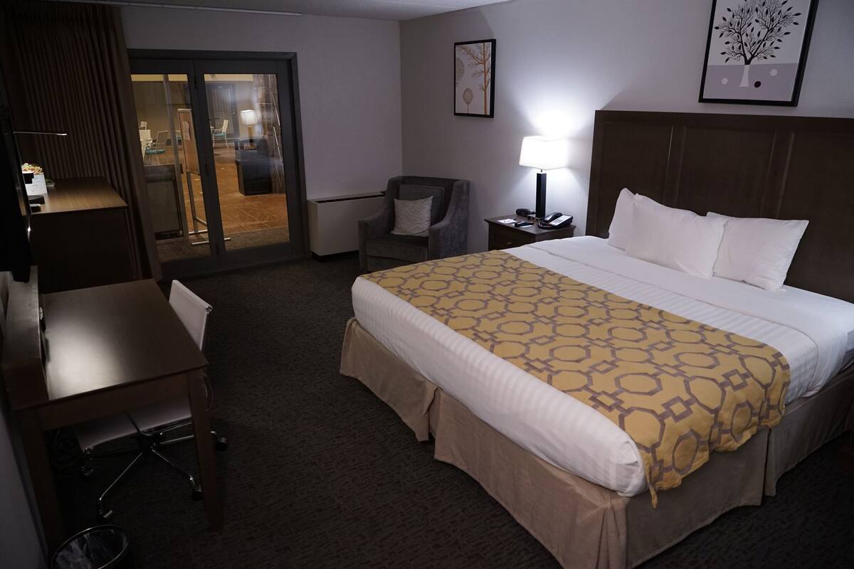 Een hotelkamer met een bed, een bureau, een stoel, een lamp en een deur naar een gang.