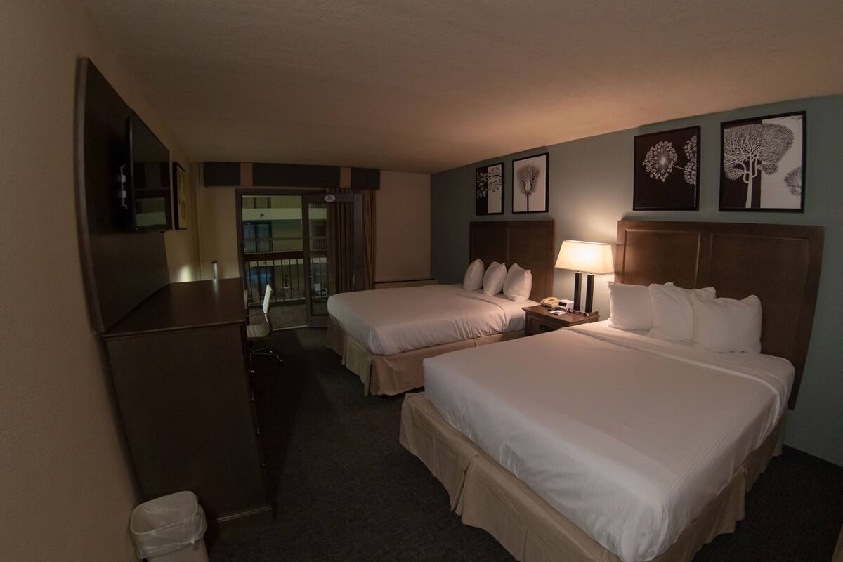 Hotelkamer met twee bedden, een bureau, een stoel, een lamp en uitzicht op het omliggende landschap.