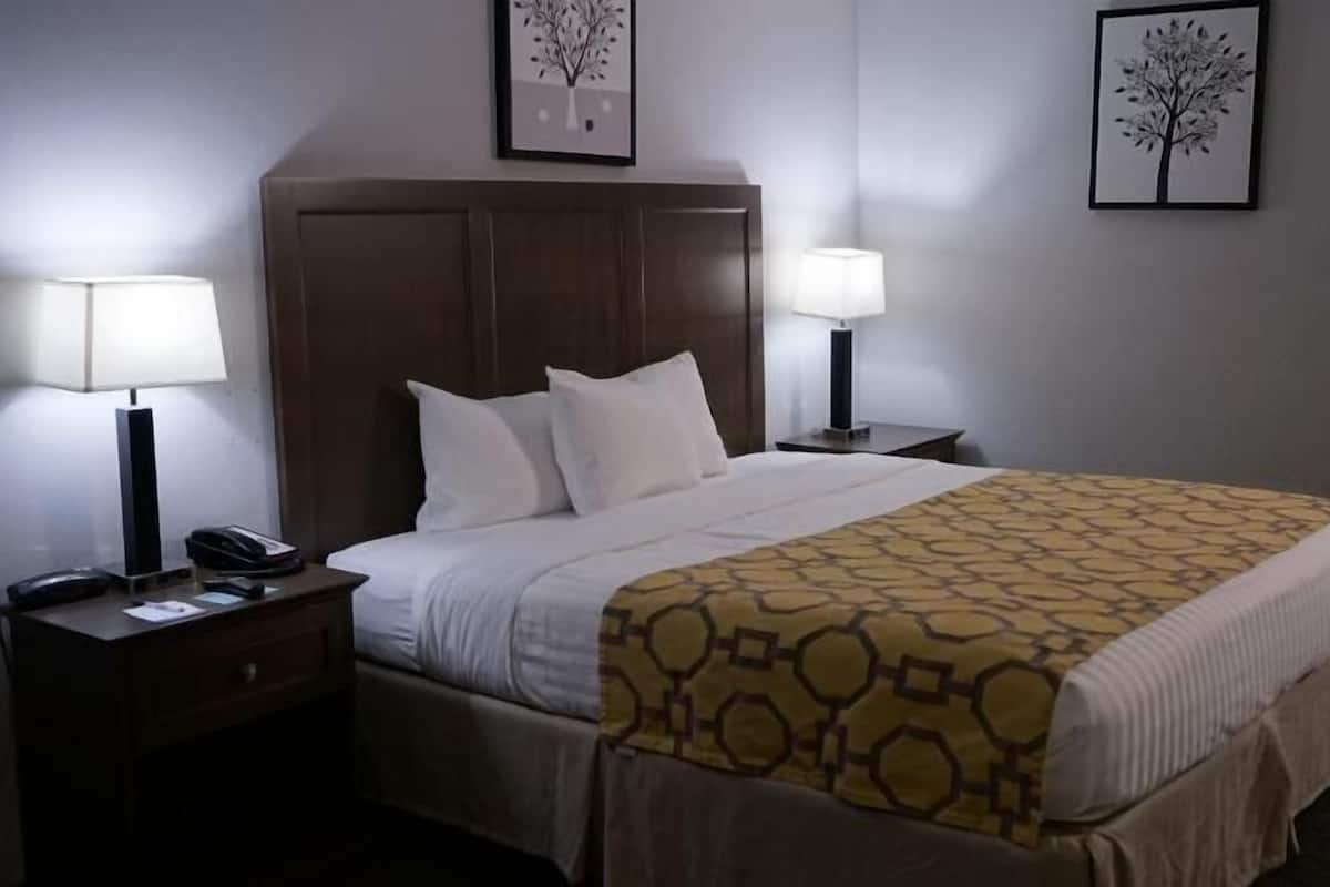Een hotelkamer met een bed, twee bedlampen, een telefoon en twee ingelijste foto's aan de muur.