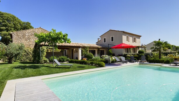 A swimming pool with a wooden deck, surrounded by a well-maintained lawn and various plants.