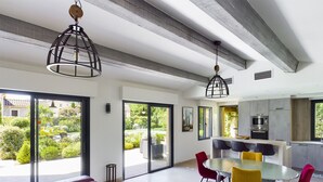 A modern kitchen with an oven and microwave, a dining area with a glass table and chairs, and a living area with red sofas and a large window.