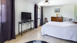 A bedroom with a bed, a TV on a stand, a dresser, and a window with curtains.