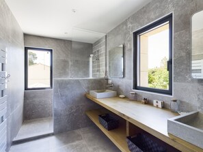 Une salle de bain moderne dotée d’une grande fenêtre, d’une douche à l’italienne et d’un meuble-lavabo avec un miroir.