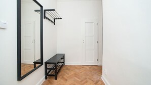 A hallway with a wooden herringbone floor, a black metal bench, a large mirror, and a black metal rack with clothes hanging. - Elegant, modern, 2-bed flat by Museum of Prague (Prague)