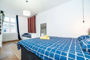 A bedroom with a large bed, a window, a radiator, and a hanging light fixture.