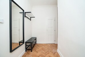 A hallway with a wooden herringbone floor, a black bench, a mirror, and a clothes drying rack.