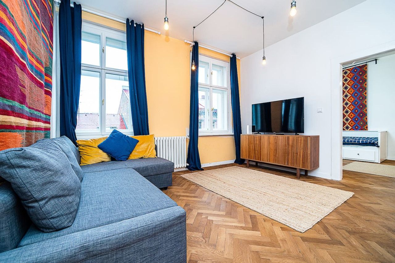 Un salon moderne avec un canapé, un téléviseur, un meuble en bois et un rideau à motifs.