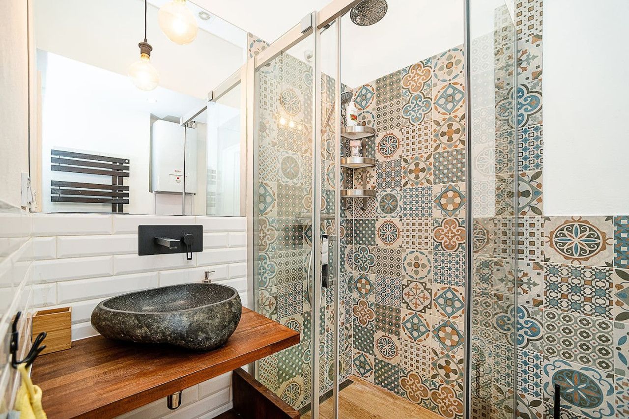 A bathroom with a stone basin, a glass shower enclosure, and patterned tiles.