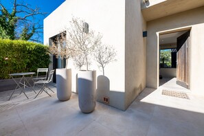 Eine moderne Terrassenanlage mit Betonboden, einem Metalltisch und Stühlen sowie großen Pflanzgefäßen.