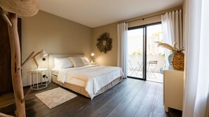 A bedroom with a large bed, a small bedside table, a lamp, a decorative wall piece, and a view of the outside through a sliding door.