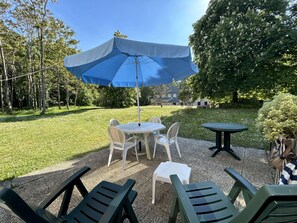 An outdoor patio with a table and chairs under a blue umbrella, surrounded by greenery and trees. - Duplex with Terrace near Beach and Shops in Saint-Pair-sur-Mer (Saint-Pair-sur-Mer)
