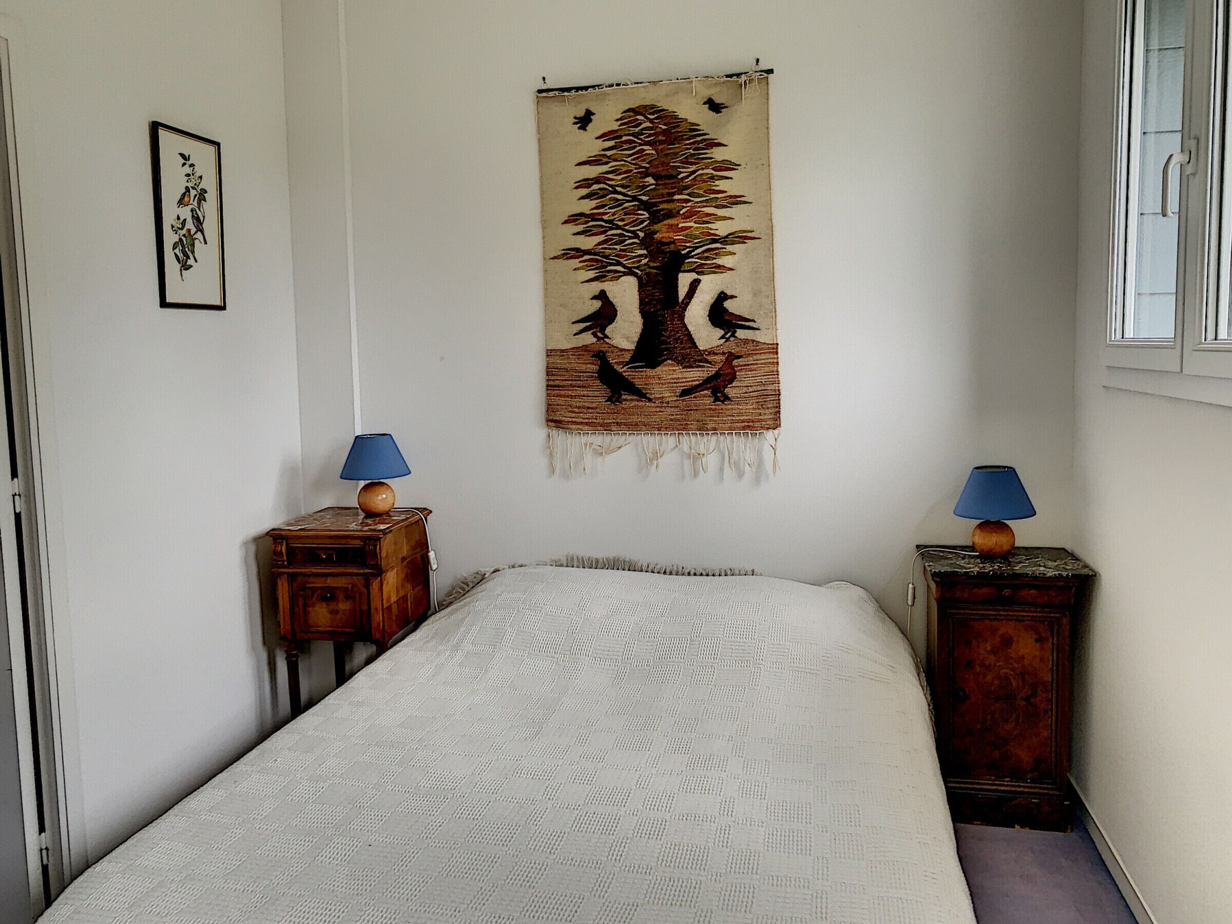 Une chambre à coucher avec un lit, deux tables de chevet avec des lampes, une tapisserie au mur et un tableau encadré.