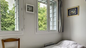 Une chambre avec un lit simple, une chaise, deux fenêtres et un radiateur.
